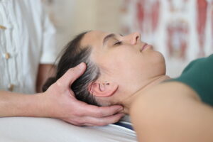 Masseur zeigt die Anwendung einer Cranio Sacralen Therapie, bei der mittels sanfter Körperberührungen die natürlichen Selbstheilungsmechanismen im Körper aktiviert werden